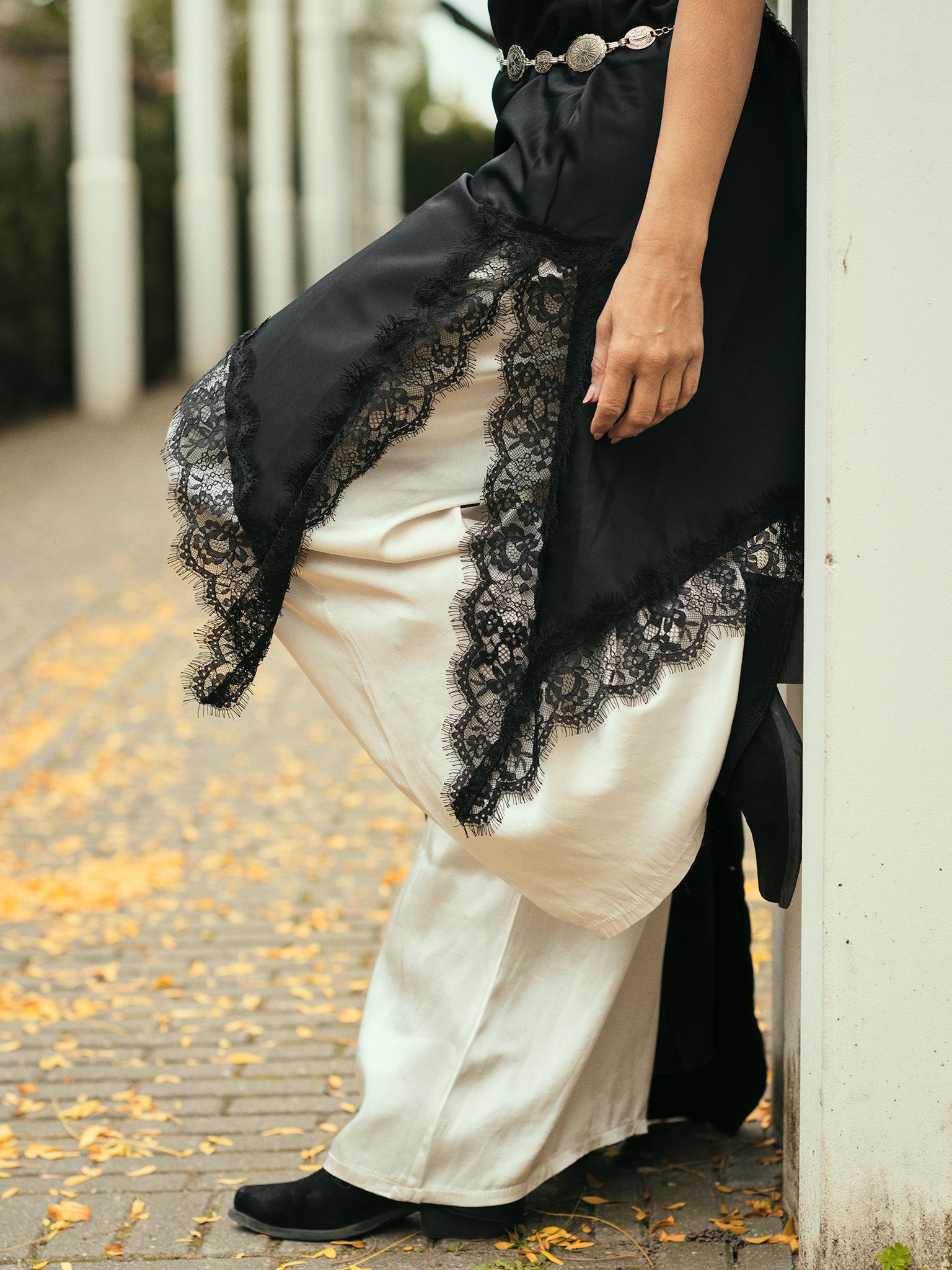 Model draagt een satijnen zwarte rok met kanten details over een witte wijde broek en zwarte laarzen elegante boho look van Tesoros de Mujer